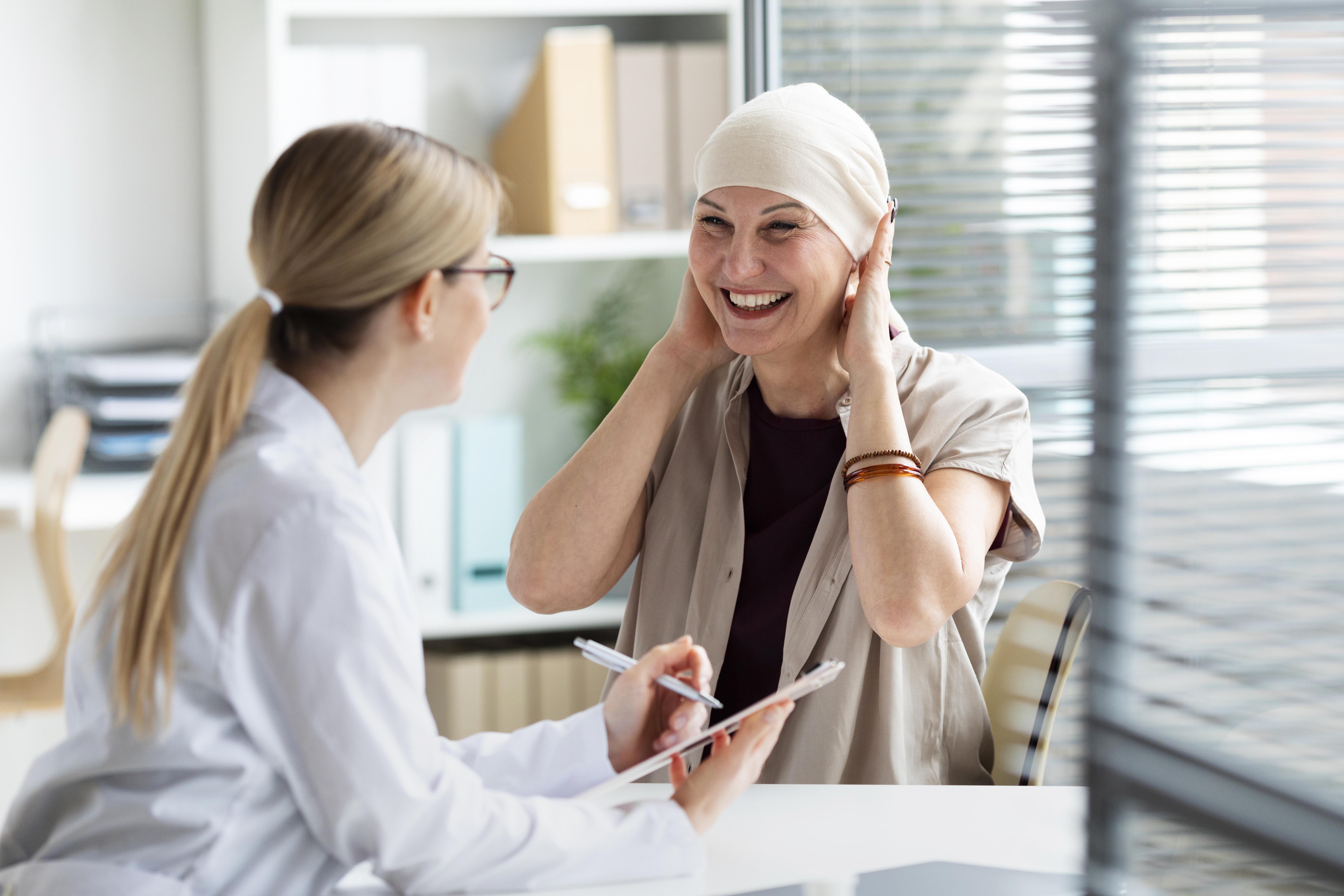 Mujer con cáncer hablando con doctora, sonriente, feliz